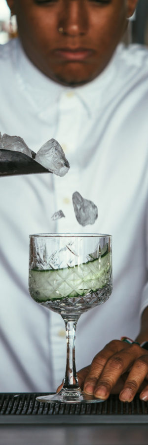 Cropped view of a mixed race male expert bartender is adding some ice cubes on a cocktail glass at the bar counter